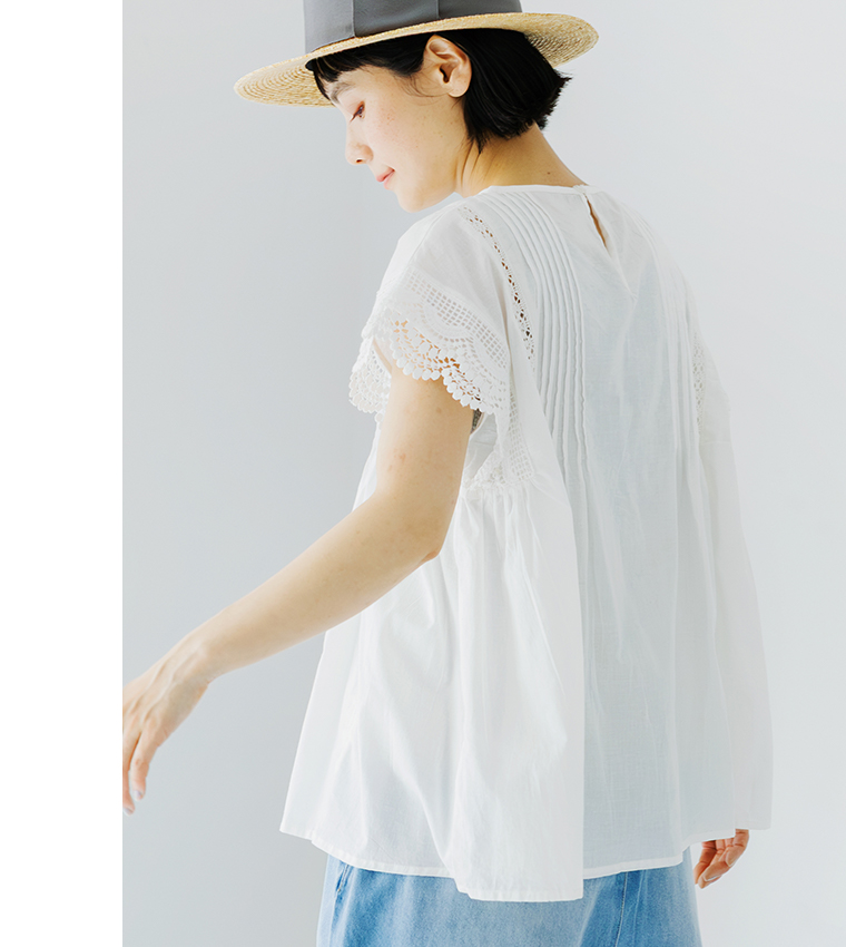 Lintu Lauluレースピンタックブラウス（ホワイト）の後ろ姿着用画像。繊細なピンタックとスカラップレース袖が特徴で、背中の小さな涙開きが上品なアクセント。麦わら帽子とライトブルーのデニムを合わせた、軽やかでナチュラルなスタイリング。