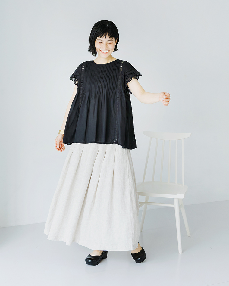 Lintu Lauluレースピンタックブラウス（ブラック）の着用コーディネート画像。繊細なピンタックとスカラップレース袖が特徴のブラウスに、ナチュラルなリネンのロングスカートを合わせたスタイリング。軽やかな素材感とモノトーンの組み合わせが上品な印象を演出。