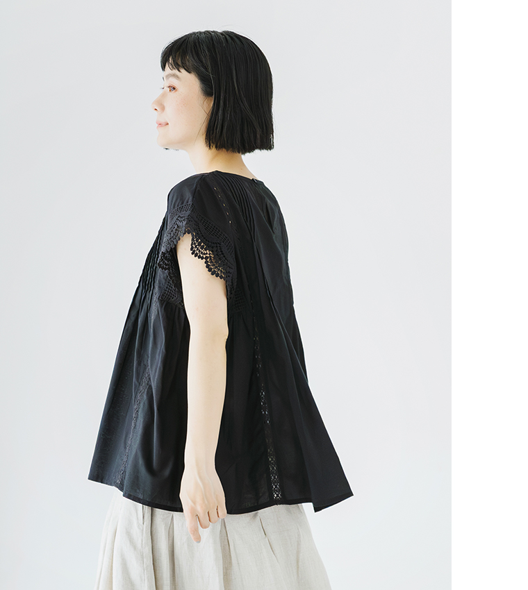 Lintu Lauluレースピンタックブラウス（ブラック）の横向き着用画像。繊細なピンタックとスカラップレース袖が特徴で、ふんわり広がるシルエットが軽やかな印象。ナチュラルなリネンボトムを合わせた上品なスタイリング。