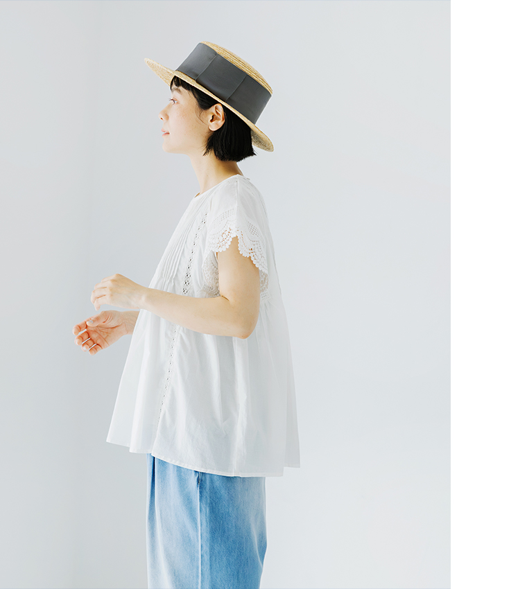 Lintu Lauluレースピンタックブラウス（ホワイト）の横向き着用画像。繊細なピンタックとスカラップレース袖が特徴で、ふんわり広がるシルエットが軽やかな印象。麦わら帽子とライトブルーのデニムを合わせた爽やかなスタイリング。