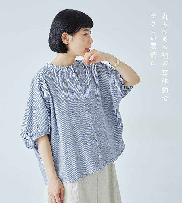 Bliss bunchのちょうちんスリーブブラウス（ブルーストライプ）を着用したモデルの横向きカット。白のサロペットに重ねたスタイリングで、ふんわりとした丸みのある袖が立体的に見えるデザイン。右側に「丸みのある袖が立体的でやさしい表情に」というテキスト入り