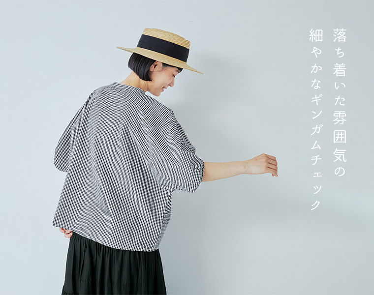  Bliss bunchのちょうちんスリーブブラウス（ブラック×ホワイトのギンガムチェック）を着用したモデルの後ろ姿。麦わら帽子をかぶり、黒のスカートを合わせたナチュラルなスタイリング。右側に「落ち着いた雰囲気の細やかなギンガムチェック」というテキスト入りで、穏やかな印象を表現したカット。
