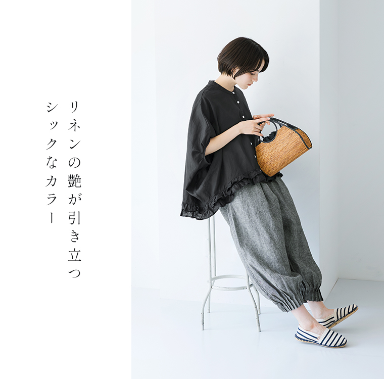 ubasokuリネン裾二段フリル前開本貝釦ブラウス（ブラック）を着用したモデルの横向きコーディネート画像。グレーのリネンパンツとストライプのフラットシューズを合わせ、ナチュラルなかごバッグを持ったスタイリング。リネンの艶が引き立つシックなカラーで、軽やかかつ上品な印象を演出。