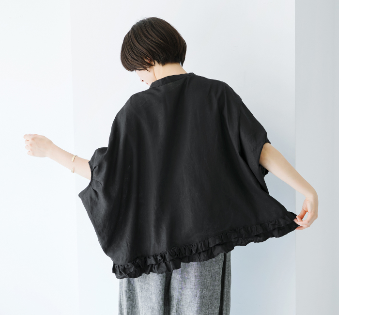 ubasokuリネン裾二段フリル前開本貝釦ブラウス（ブラック）のバックシルエット画像。モデルが腕を広げて立ち、裾の二段フリルがふんわりと広がる様子が見える。リネン素材の自然な艶と軽やかなドレープ感が際立つ後ろ姿。