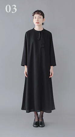 Luuna miu【慶弔両用】大切な日のボウタイAラインワンピース着用イメージ。黒のロングワンピースを着たモデルがグレー背景の前に立ち、首元にリボンディテールがあしらわれた上品なデザインが見える商品画像。フォーマルシーンにふさわしい落ち着いた印象。