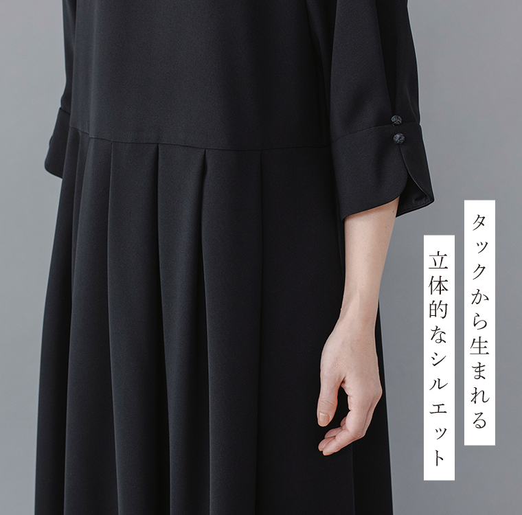 Luuna miu【慶弔両用】大切な日のジャケット＆ワンピースセットのディテールイメージ。黒のワンピースのウエストから裾にかけて入ったタックが立体的なシルエットを生み出している様子を写した写真。袖口には編みボタンがあしらわれ、右側には「タックから生まれる 立体的なシルエット」という日本語テキストが添えられた商品画像。
