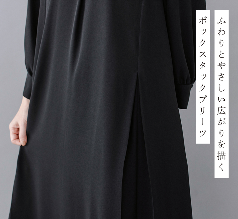Luuna miu【慶弔両用】大切な日のボタンフレアワンピースのディテールイメージ。黒のワンピースの裾部分をクローズアップし、ふんわりと広がるボックスタックプリーツの柔らかなラインが見える。袖口にはくるみボタンがあしらわれ、右側には「ふわりとやさしい広がりを描く ボックスタックプリーツ」という日本語テキストが添えられた商品画像。