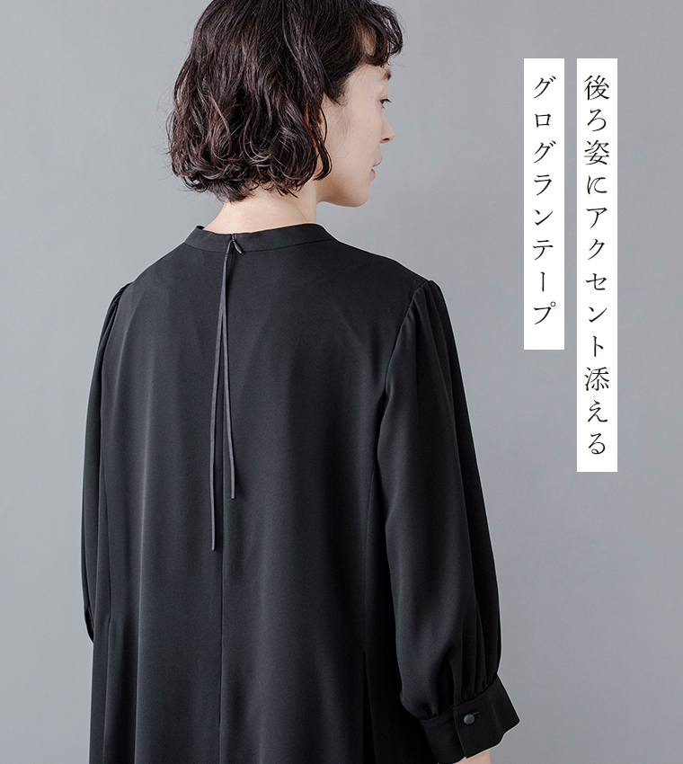 Luuna miu【慶弔両用】大切な日のボタンフレアワンピースの後ろ姿ディテール。黒のワンピースを着たモデルが背中を見せるカットで、首元から垂れるグログランテープがアクセントになっている。袖口にはくるみボタンがあしらわれ、右側には「後ろ姿にアクセント添える グログランテープ」という日本語テキストが添えられた商品画像。
