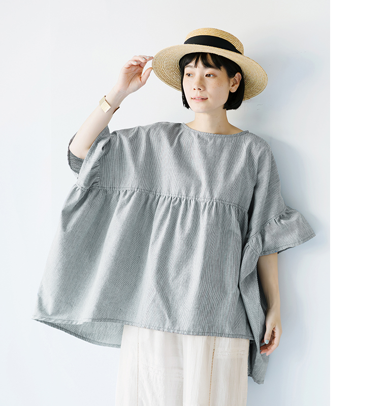 Sorte cuffぜいたくギャザーワイドブラウス（ヒッコリー）を着用した女性の正面コーディネート。細かなヒッコリー柄の生地と袖のギャザーが特徴で、麦わら帽子を合わせた軽やかなスタイリングの商品画像。