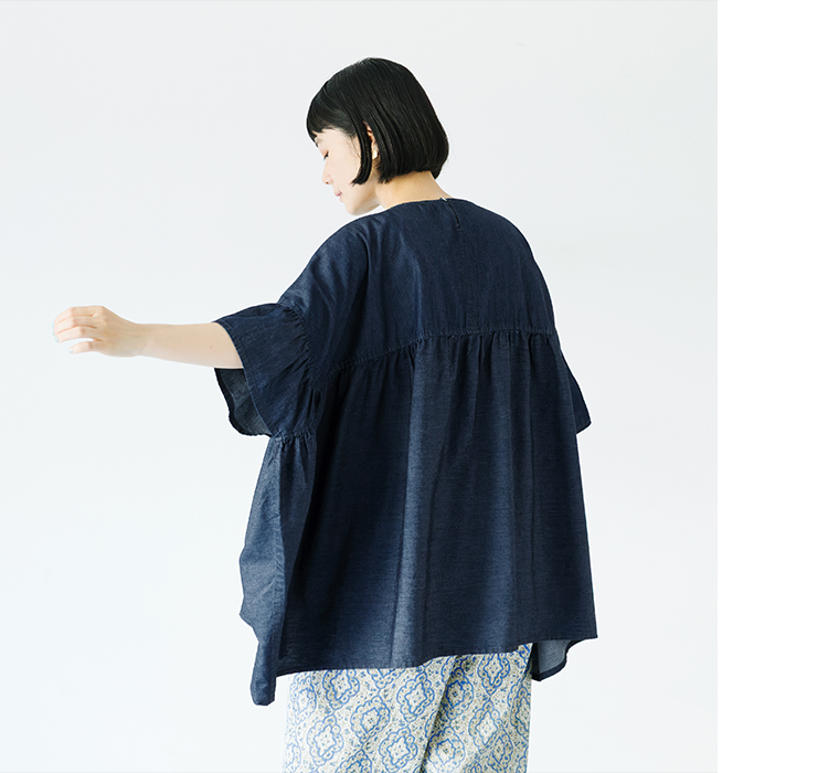 Sorte cuffぜいたくギャザーワイドブラウス（インディゴ）を着用した女性の後ろ姿コーディネート。ふんわりと広がるギャザーと軽やかな素材感が特徴で、ゆったりとしたシルエットが涼しげな印象を与える商品画像。