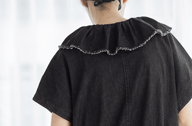 &yarn 滝口和代さんコラボ　or frill all in oneのバックディテール。黒のフリル襟が肩まわりを包み込むように広がり、切りっぱなしの端が軽やかなニュアンスを添えるデザイン。素材の質感とフリルの立体感が際立つ後ろ姿のアップ画像。