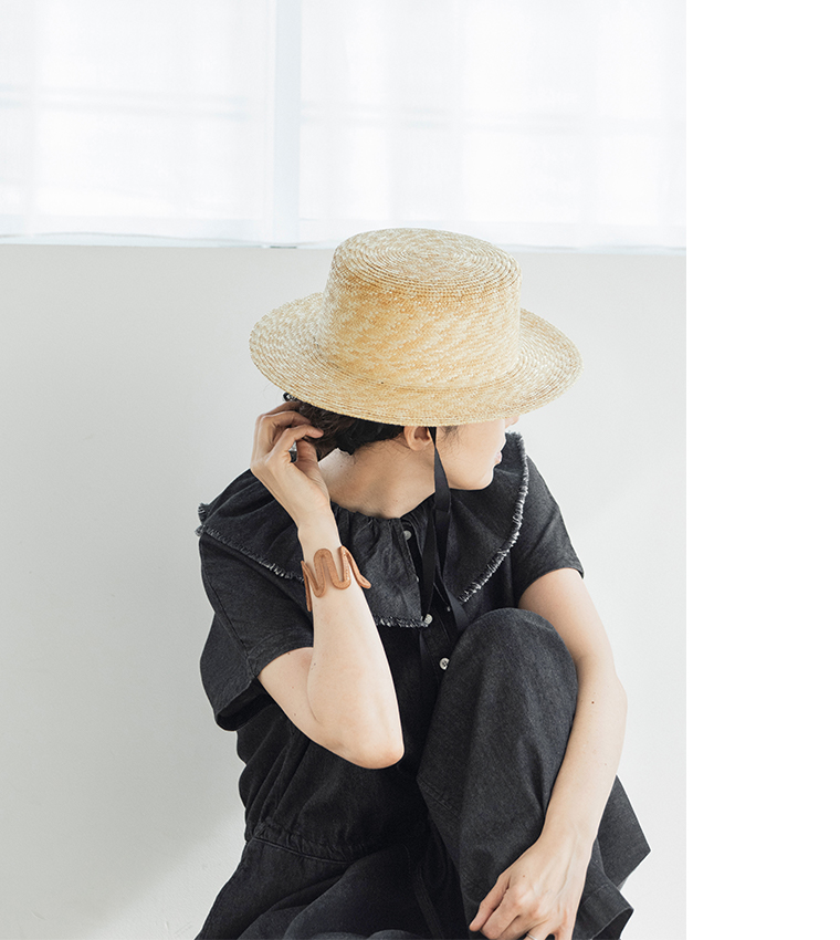 &yarn 滝口和代さんコラボ　or frill all in oneを着用したイメージ。黒のフリル付きオールインワンに麦わら帽子を合わせ、軽やかでナチュラルな雰囲気を演出。座った姿勢から素材の柔らかさとリラックス感が伝わる商品画像。