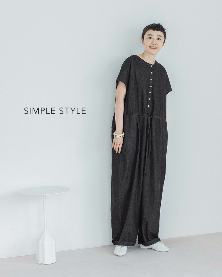 &yarn 滝口和代さんコラボ　or frill all in oneを着用したイメージ。黒のオールインワンをシンプルに着こなし、白いシューズとバングルを合わせたスタイル。ミニマルな空間でナチュラルな雰囲気を引き立てる商品画像。
