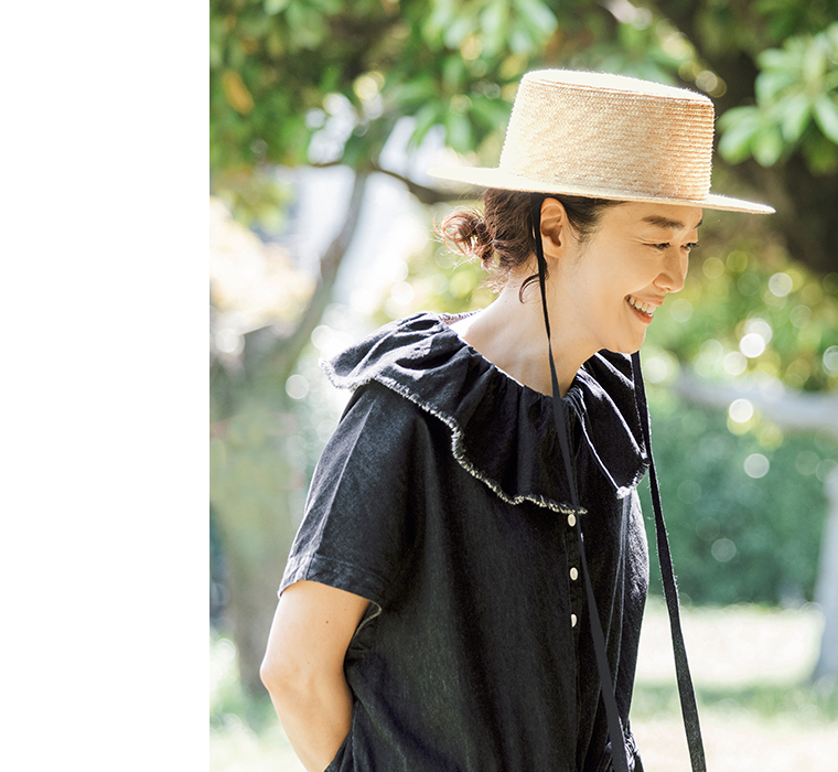 田中帽子店 滝口和代さん×田中帽子店コラボ quiet straw hat の着用イメージ。黒いリボン付きの麦わら帽子をかぶった人物が屋外で微笑む横向きカット。自然光に照らされた帽子の質感と黒のワンピースのコントラストが美しいスタイリング写真。