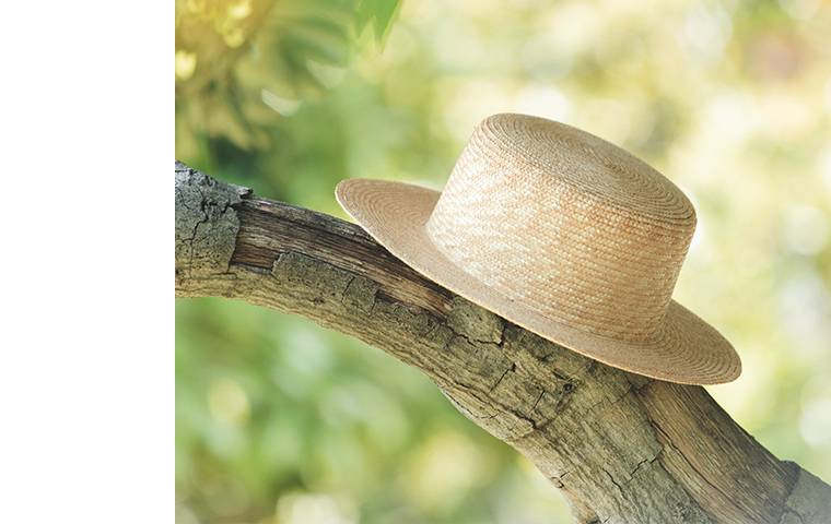 田中帽子店 滝口和代さん×田中帽子店コラボ quiet straw hat の商品ディテール。自然光の中、木の枝に麦わら帽子が掛けられている様子。編み目の美しい質感と穏やかな光が調和した、ナチュラルな雰囲気のイメージカット。