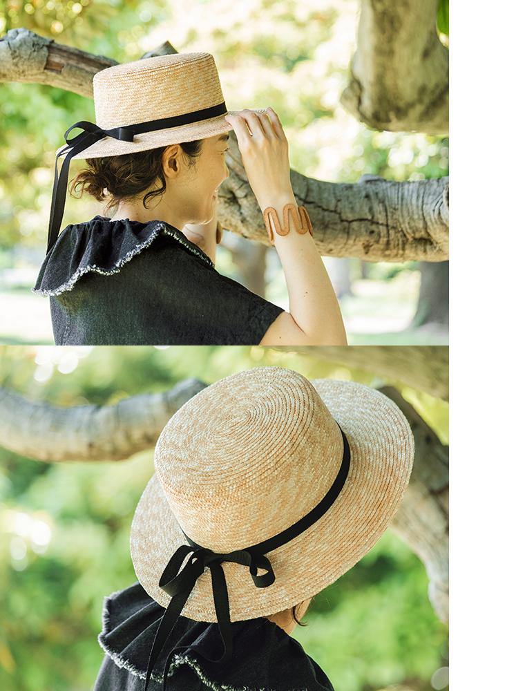 田中帽子店 滝口和代さん×田中帽子店コラボ quiet straw hat の着用ディテール。黒いリボンを結んだ麦わら帽子をかぶった人物が、木の枝に手を添えて微笑む横向きカットと、後ろ姿で帽子の編み目とリボンの結び目が見えるカット。自然光に照らされた穏やかな雰囲気が伝わるスタイリングイメージ。