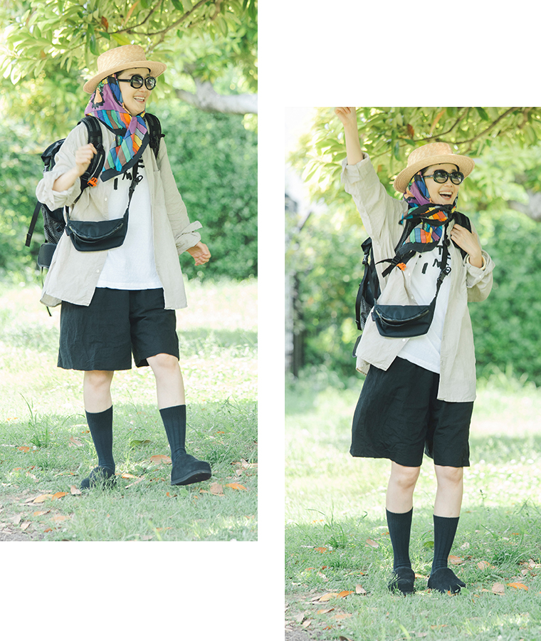 田中帽子店 滝口和代さん×田中帽子店コラボ quiet straw hat の着用イメージ。麦わら帽子にカラフルなスカーフを合わせ、サングラスとリネンシャツ、黒のショートパンツを着た人物が屋外で軽やかに動く姿。バックパックとポーチを合わせたアクティブなフェススタイルで、自然の中の明るい雰囲気を表現したカット。
