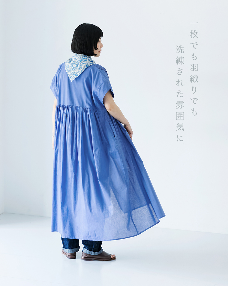 Noiaキャンブリックボイル前開きピンタックワンピース（ブルー）にデニムパンツと柄スカーフを合わせた女性の後ろ姿。ギャザーによるふんわりとしたバックシルエットの全身カットで、「一枚でも羽織りでも 洗練された雰囲気に」のコピーテキストが入った画像。