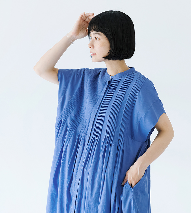 Noiaキャンブリックボイル前開きピンタックワンピース（ブルー）を着用した女性の上半身カット。右手を頭に添え、左手をポケットに入れながら斜め横を向いているポーズの画像。