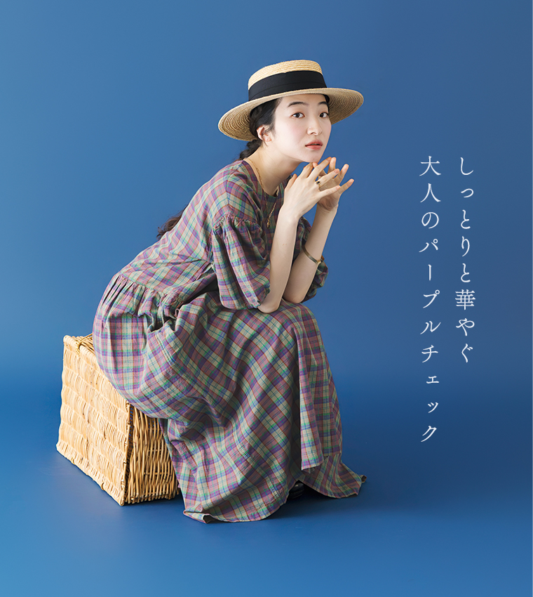Lintu Lauluマドラスチェックワンピース（パープル系）に麦わら帽子を合わせたコーディネート。青い背景で、カゴバッグの上にしゃがみ込み、顎を手に乗せて上を見上げる女性のカット。「しっとりと華やぐ 大人のパープルチェック」のコピーが添えられている