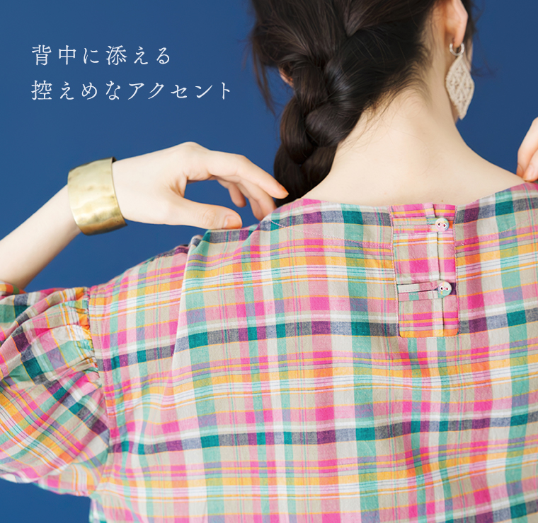 Lintu Lauluマドラスチェックワンピース（ピンク系）のバックスタイルディテール。青い背景で、後ろを向いた女性の首元のボタンデザインに焦点を当てたアップカット。「背中に添える 控えめなアクセント」のコピーが添えられている