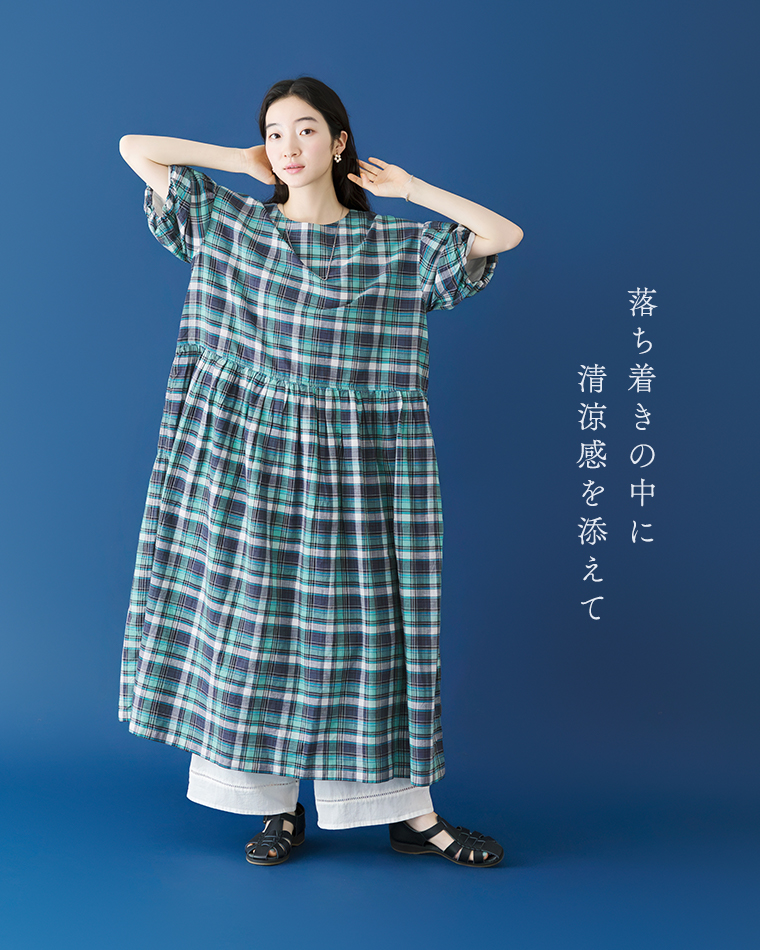 Lintu Lauluマドラスチェックワンピース（ブルー系）に白のワイドパンツと黒のサンダルを合わせたコーディネート。青い背景で、両手を頭の後ろに添えて正面を向く女性の全身カット。「落ち着きの中に 清涼感を添えて」のコピーが添えられている