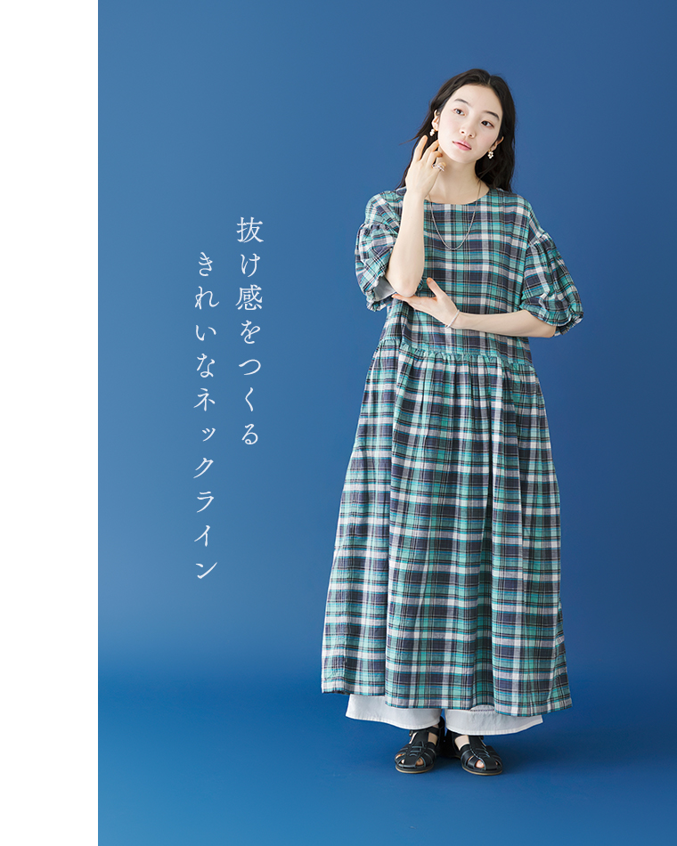 Lintu Lauluマドラスチェックワンピース（ブルー系）に白のワイドパンツと黒のサンダルを合わせたコーディネート。青い背景で、右手をフェイスラインに添えて佇む女性の全身カット。「抜け感をつくる きれいなネックライン」のコピーが添えられている