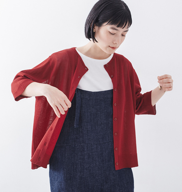 &yarn5分袖ニットカーディガン（レッド）の前を開けて羽織り、デニムのサロペットを合わせた、斜めを向いた正面アップの着こなしイメージ画像