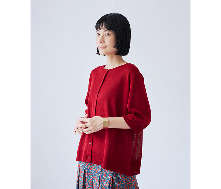 &yarn5分袖ニットカーディガン（レッド）のボタンを留めてプルオーバー風に着こなし、手元を組んだ斜め正面のアップ画像
