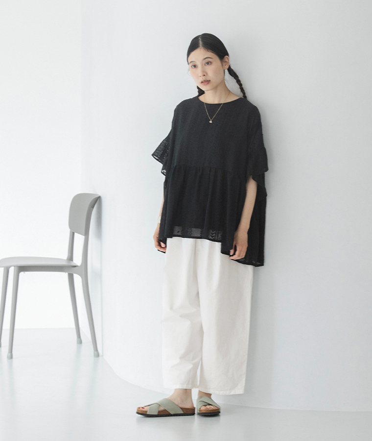 ブラックのシアー刺繍プルオーバーに白パンツを合わせた女性モデルの全身スタイル