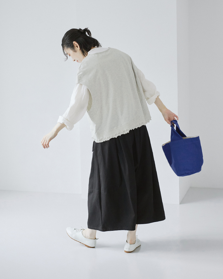 le ciel a temps douxミニミニ裏毛 裾メローTシャツベスト（オートミール）を白シャツに重ね、黒のスカートとブルーのバッグを合わせたコーディネートのバックスタイル画像。