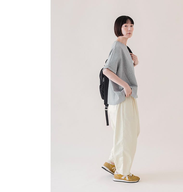杢グレーのカットベストを白のパンツと黒のリュックに合わせた、サイドシルエットがわかる着用画像