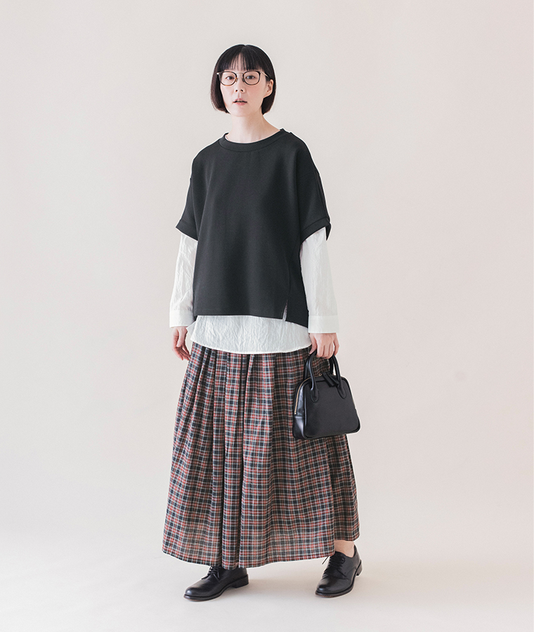 ブラックのカットベストに白シャツとチェック柄スカートを合わせ、黒のバッグを持った全身コーディネート画像
