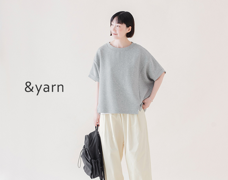 &yarnの杢グレーのカットベストを白のパンツとスニーカーに合わせ、黒のリュックを背負った全身コーディネート画像