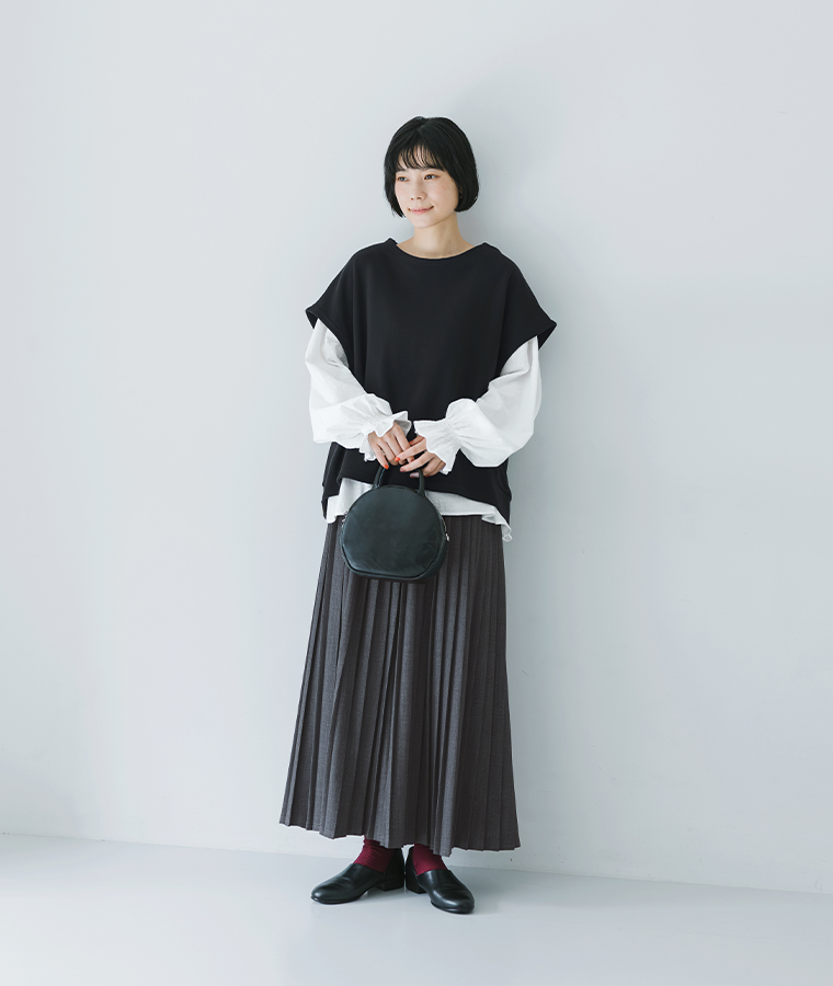 白ブラウスに黒ベストを重ねた女性モデルのレイヤードスタイル