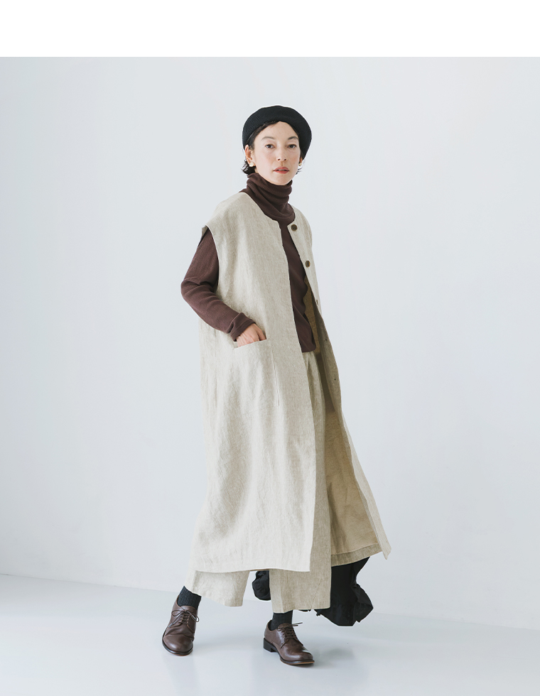 グレージュのロングベストの前を開けて歩く女性モデル