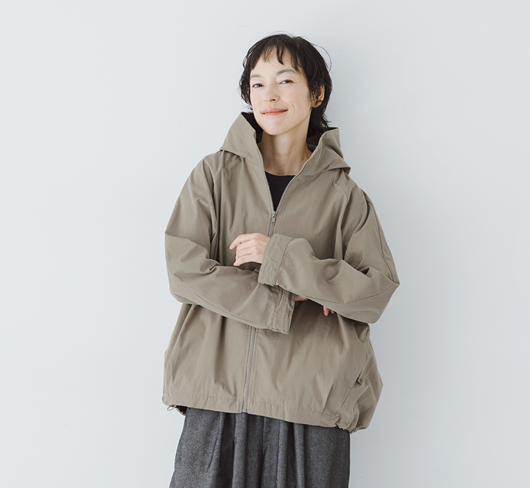 グレーベージュのフードZIPジャケットを着用し、ゆったりとした袖やシルエットを見せたモデルの正面上半身カット
