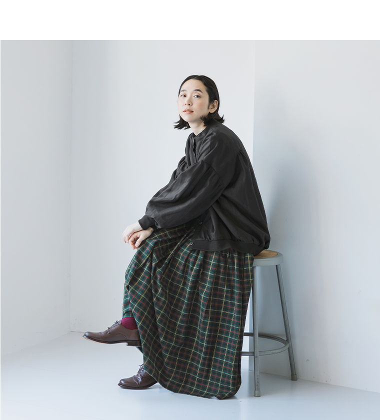 リネンリブ付きブラウス（ブラック）を着用して椅子に座る女性モデル