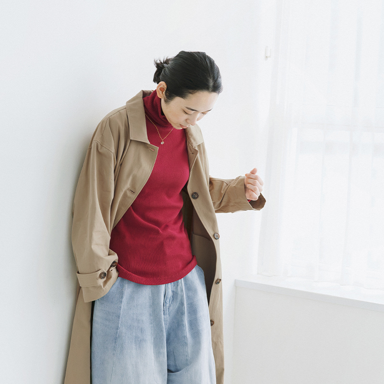 レッドのタートルネックにベージュのコートとデニムパンツを合わせた着こなし