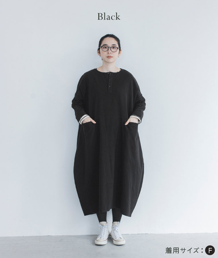 ブラックのコクーンワンピースにタイツと白いハイカットスニーカーを合わせた女性モデル