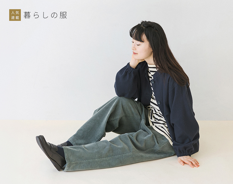 暮らしの服　コーデュロイワークストレートパンツのグリーンをネイビーのジャケットとボーダートップスに合わせたモデルの座り姿
