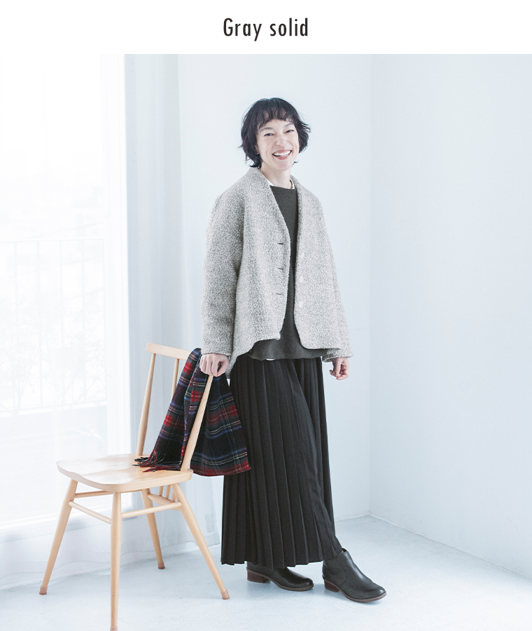 グレーのノーカラージャケットと黒のプリーツスカートを合わせた女性モデル