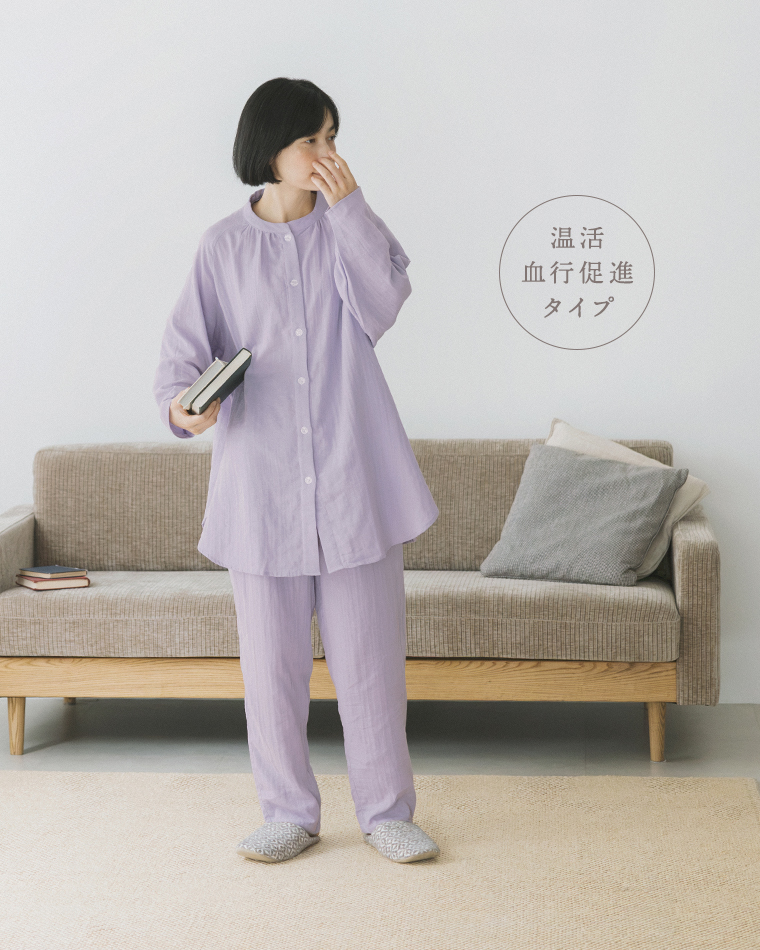 着る保湿クリーム(R)×TERAX 温活・血行促進パジャマ（パープル）の着用イメージ。ソファの前で本を持って立つコーディネート
