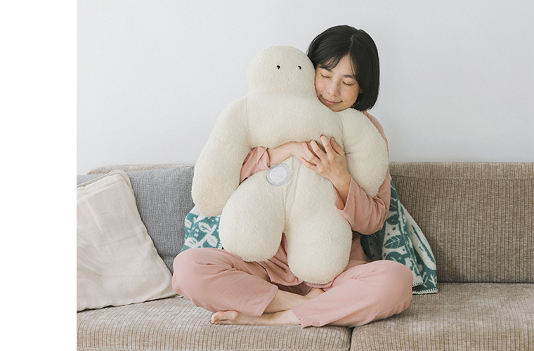 着る保湿クリーム(R) 前開きテーラーカラーパジャマ（ピンク）を着用し、ぬいぐるみを抱えながらソファでくつろぐおやすみ前のイメージ