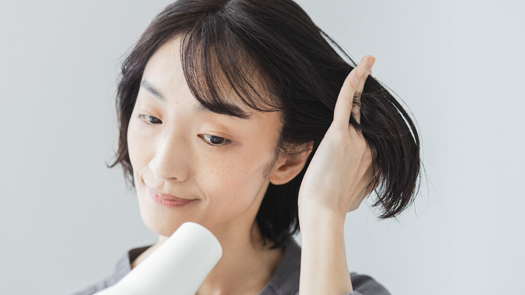 ドライヤーで髪の根元を乾かす女性