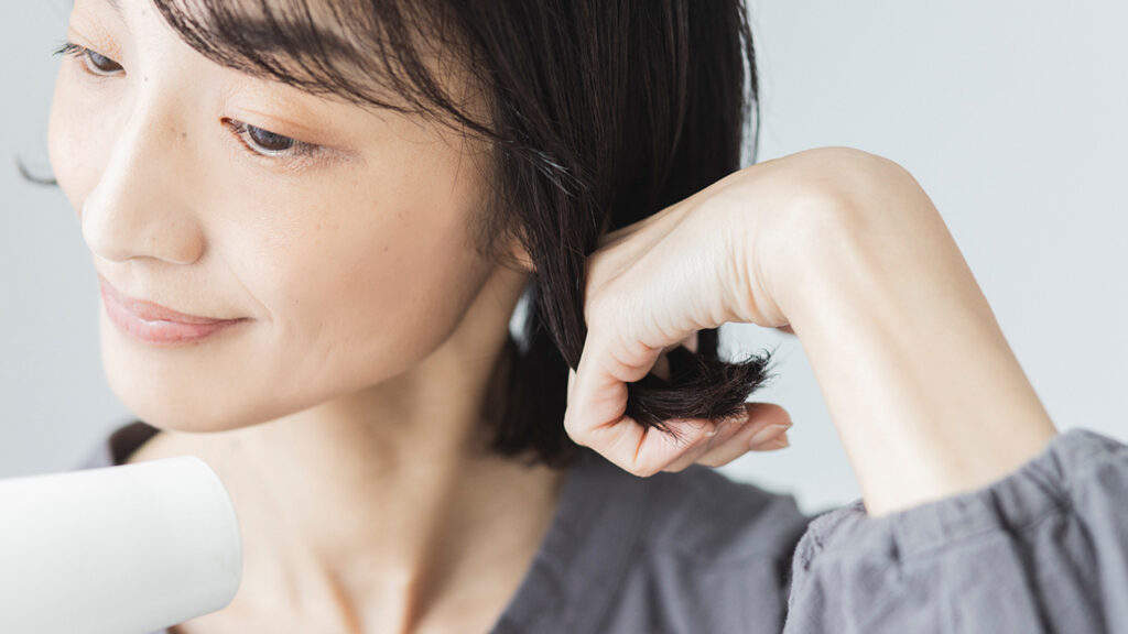 手で裾の髪をカールさせながら乾かす女性